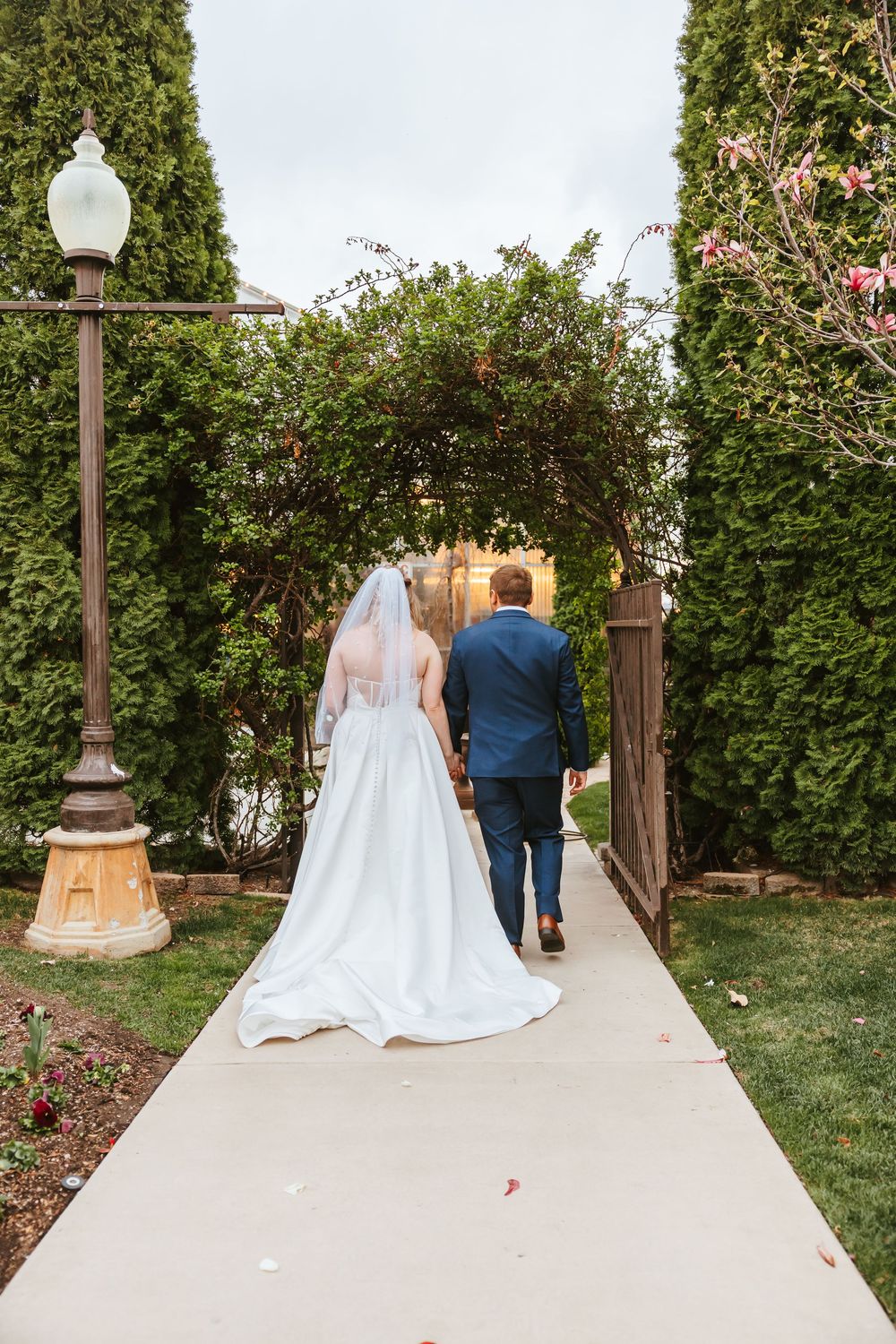 Couple walking down garden path under flowering archway with vintage lamp post.