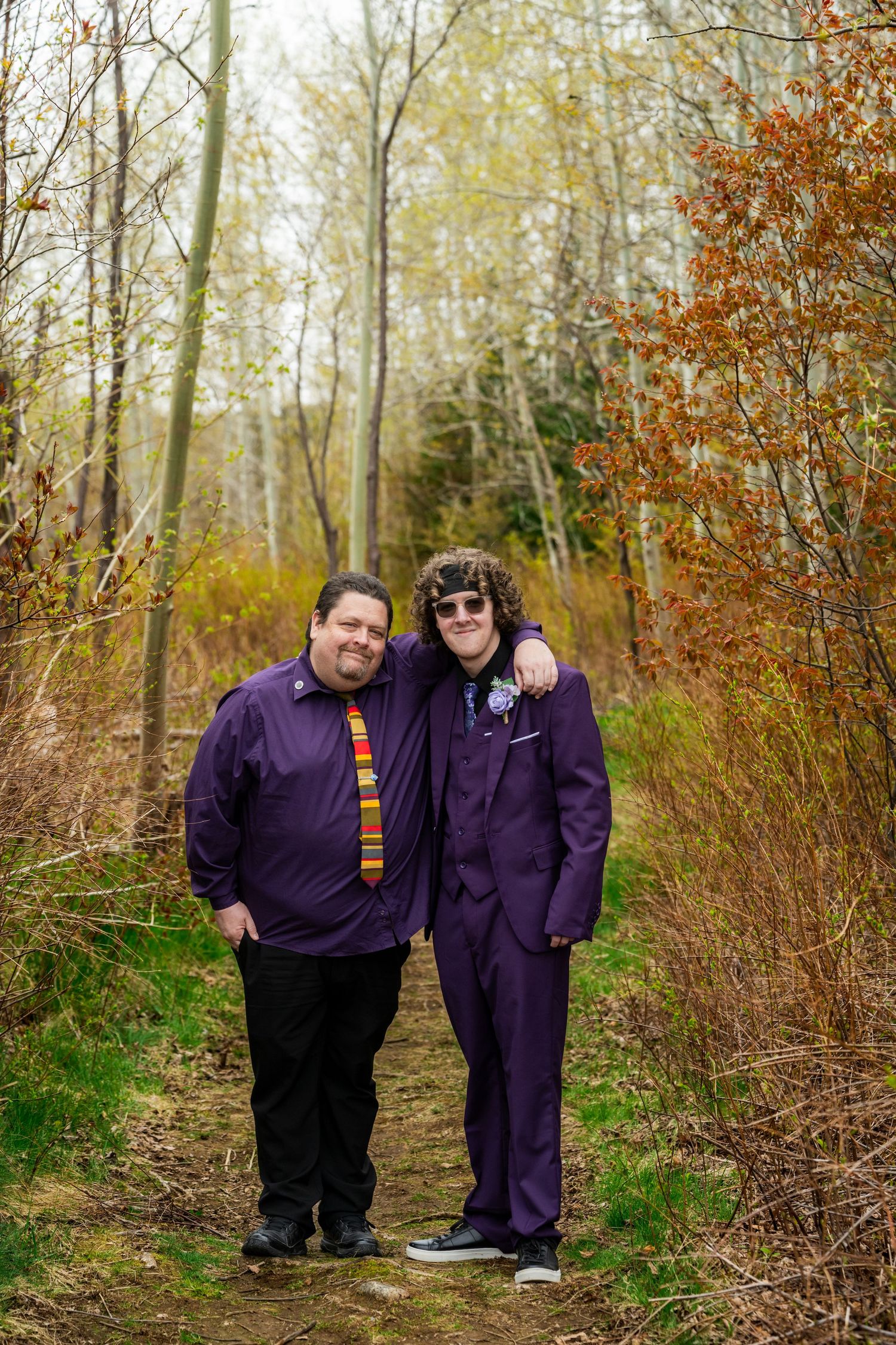 Two people wearing matching purple outfits standing together on a forest trail during autumn.