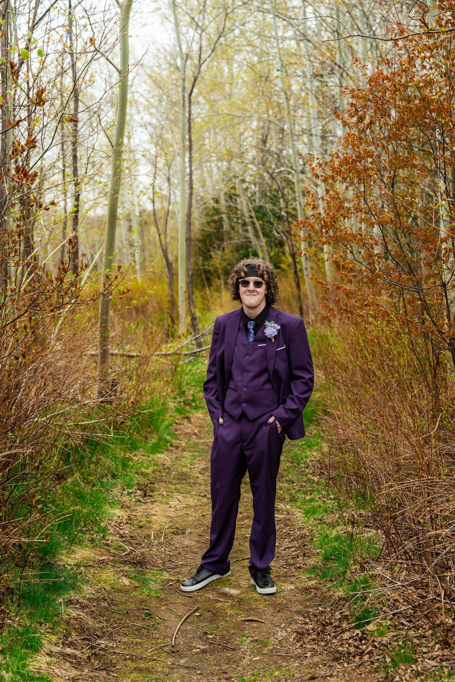 Someone wearing a purple tracksuit stands on a forest trail surrounded by autumn foliage and bare trees.