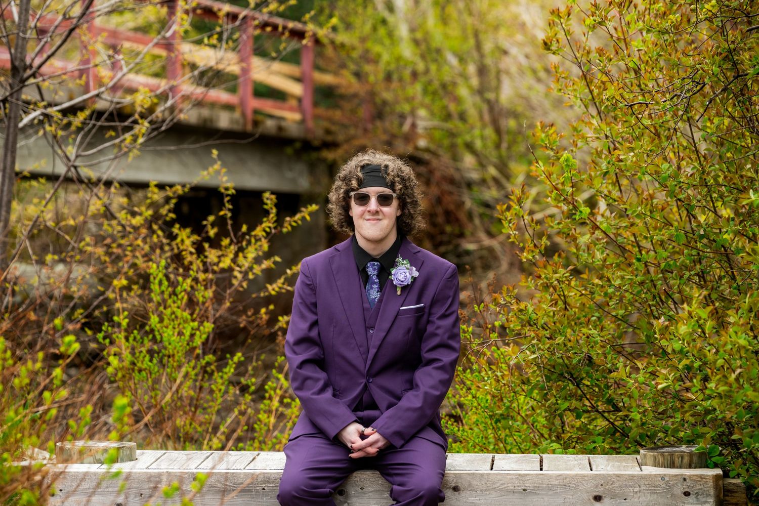 Someone in a royal purple suit sits on a bench surrounded by autumn foliage and leaves.