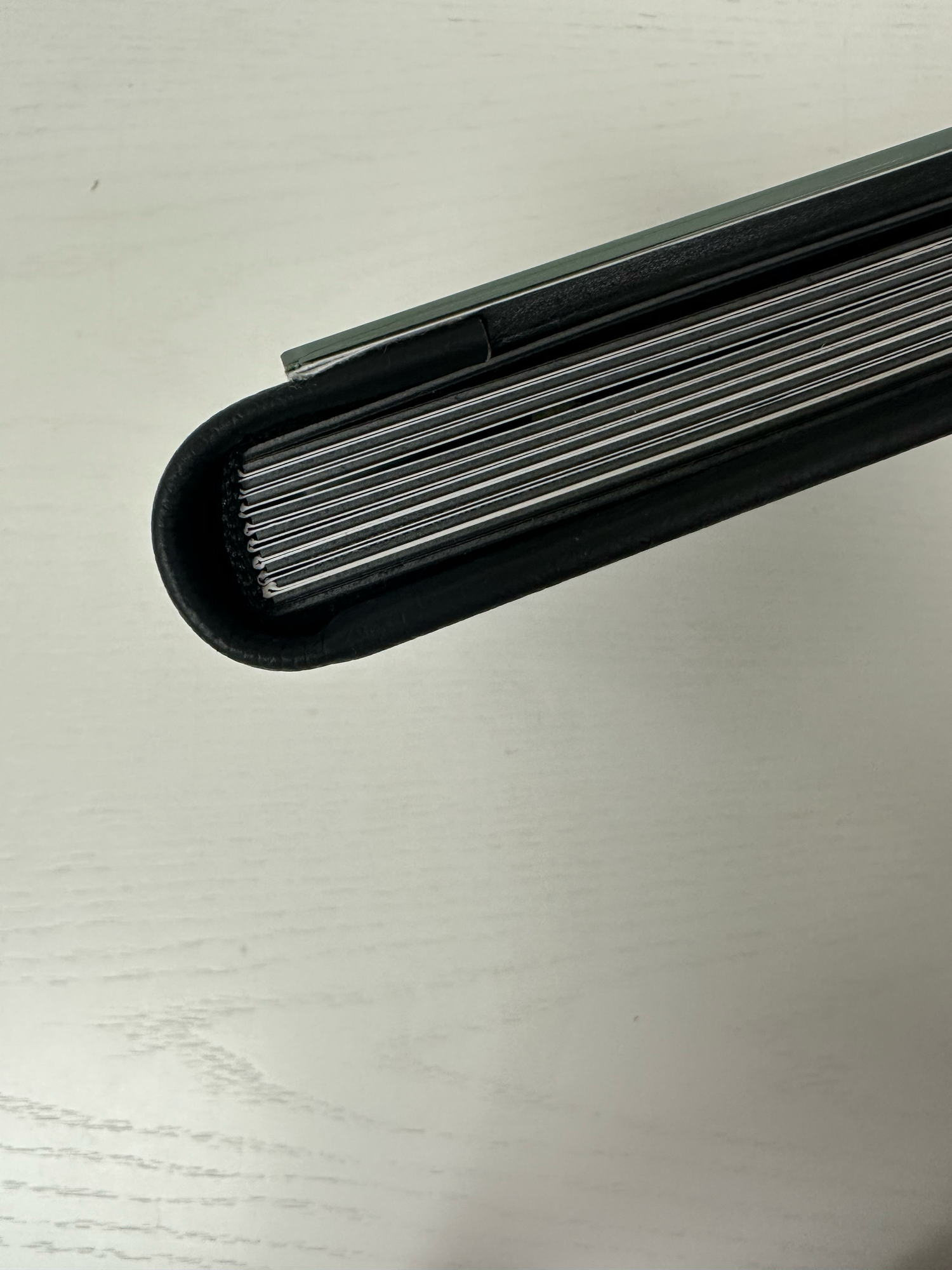 Close-up of a black hardcover photo album spine showing multiple pages on a white surface. Photo book