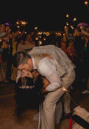 Bride and groom sharing a passionate dip kiss surrounded by guests holding sparklers at night celebration.