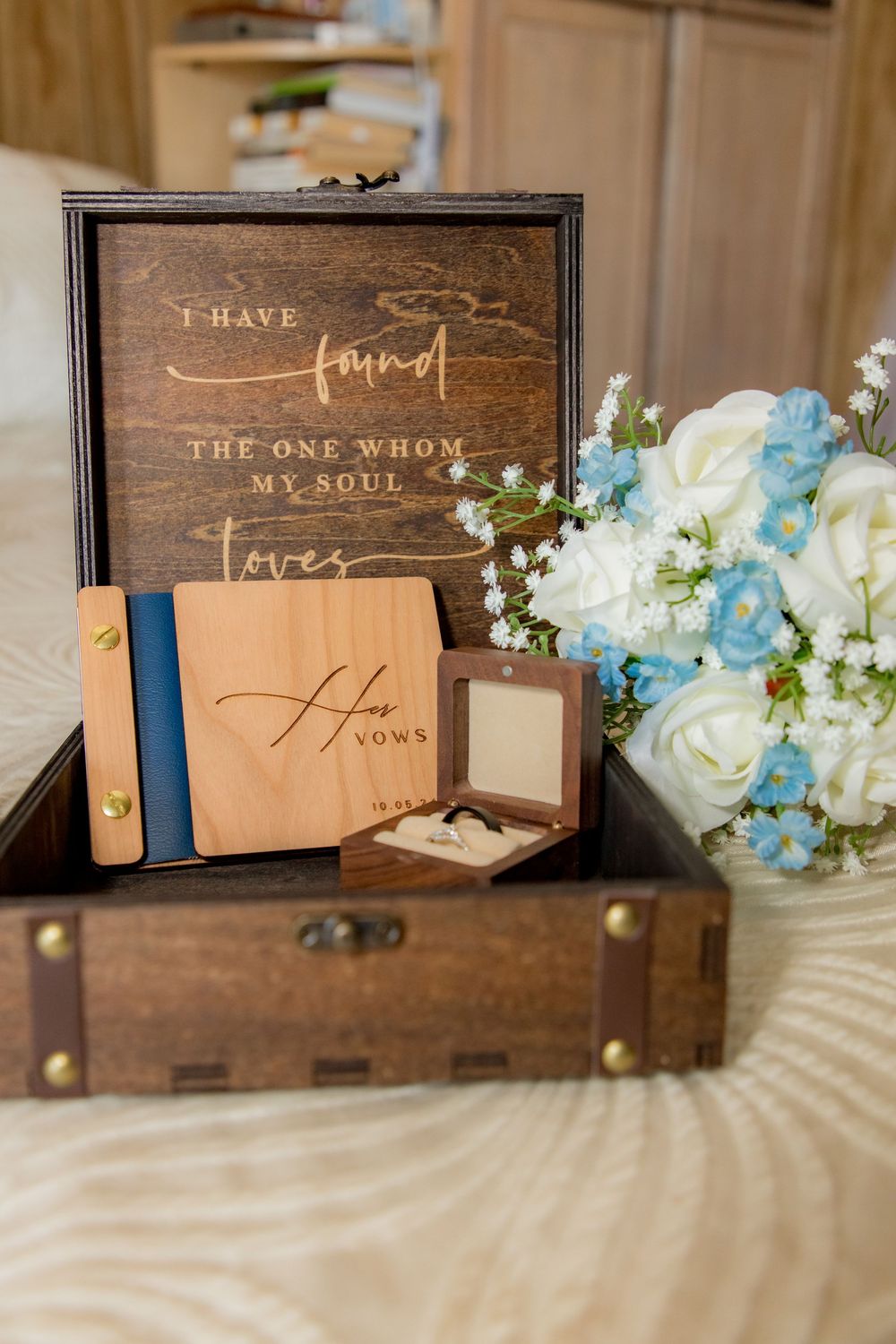 Wooden wedding keepsake box with vow books, ring box, and white and blue floral bouquet arrangement.