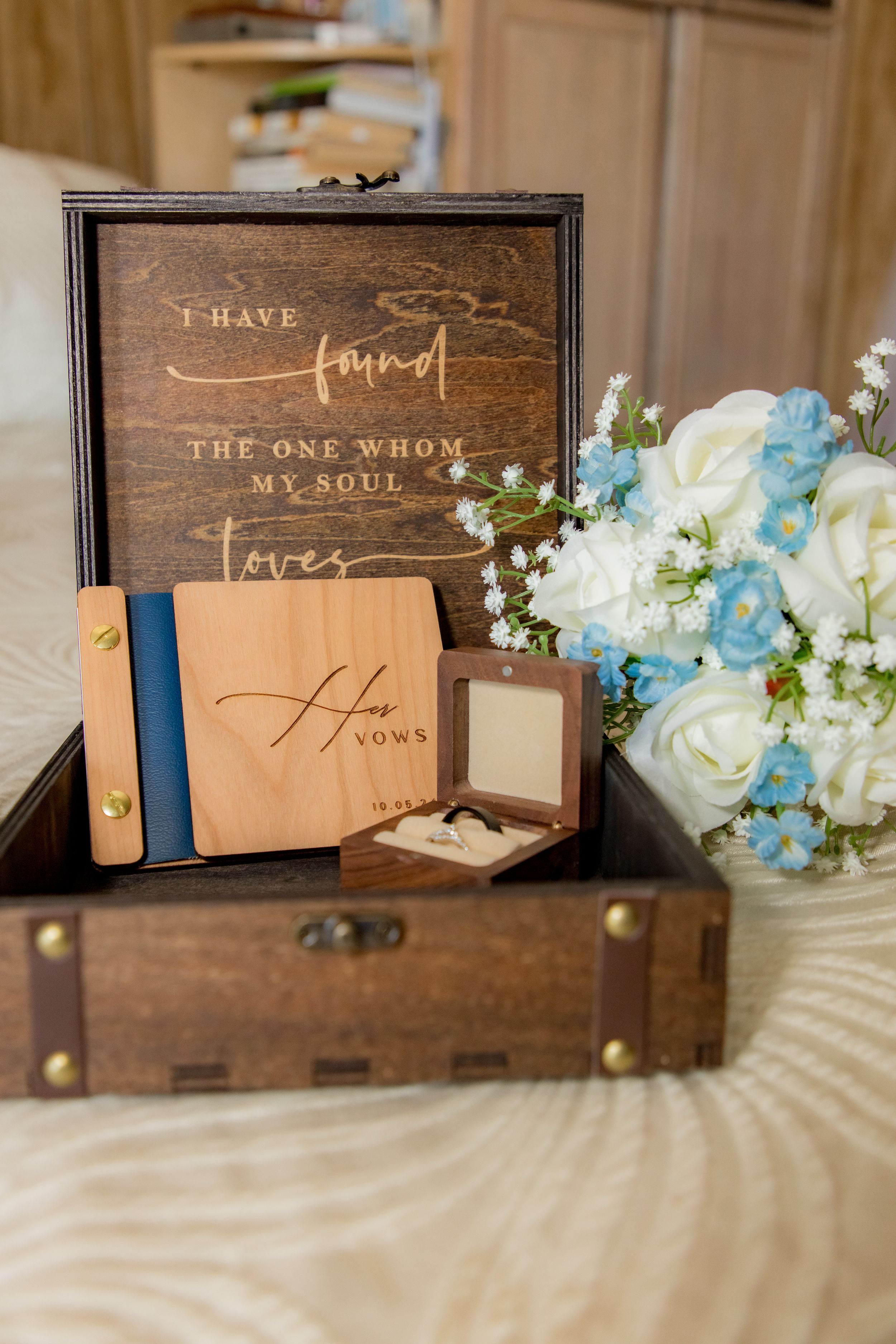 Wooden wedding keepsake box with vow books, ring box, and white and blue floral bouquet arrangement.