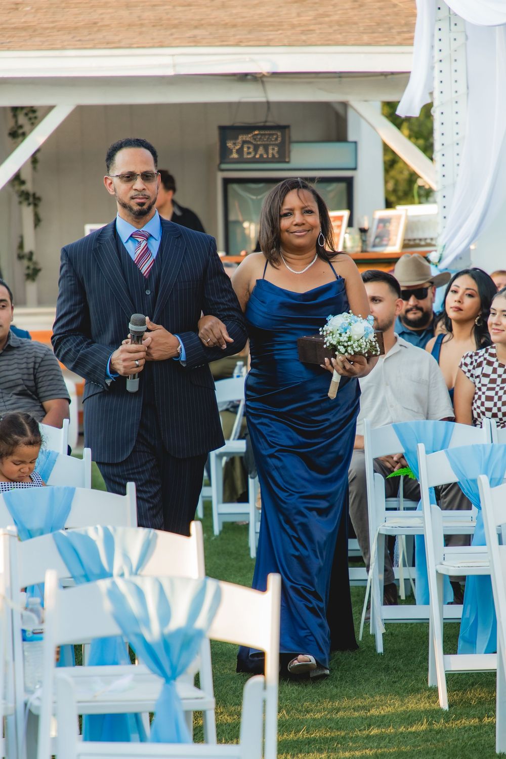 Bridesmaid in blue gown and groomsman walking down the aisle at an outdoor wedding ceremony.