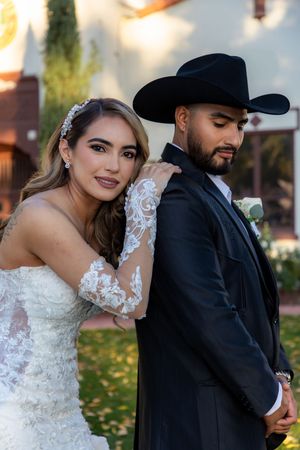 Elegant bride in lace gown leans on grooms shoulder, groom wearing black cowboy hat and suit.