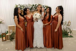 Bride in white lace gown poses with four bridesmaids in rust-colored satin dresses at wedding.