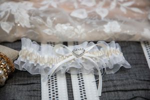 White ruffled bridal garter with heart-shaped rhinestone charm displayed on gray striped fabric.