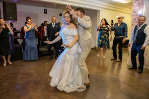 Bride in lace wedding gown dancing with groom at wedding reception surrounded by guests.