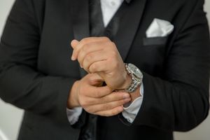Close-up of a groom in a black suit adjusting his cufflinks, wearing a silver watch.