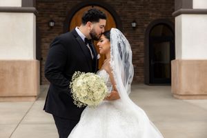Newlyweds share an intimate forehead touch outside a brick church, bride in ballgown holding white bouquet.