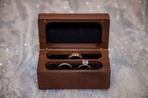 Two gold wedding bands and diamond engagement ring displayed in a wooden ring box.