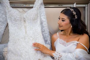 Bride admires intricate beaded lace wedding dress hanging on rack before getting dressed.