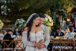 Bride and groom sharing a joyful embrace during outdoor wedding ceremony with white floral arrangements.