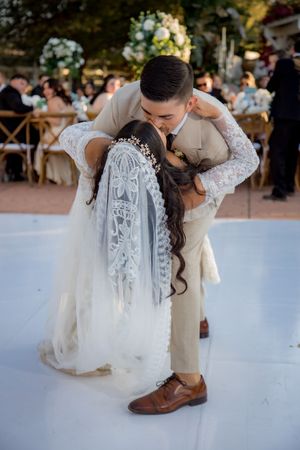 Groom dips bride for a romantic kiss on the white dance floor at an outdoor wedding reception.
