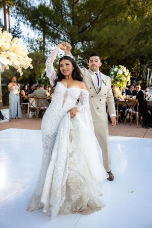 Bride and groom celebrate joyfully on white dance floor at elegant outdoor wedding reception.
