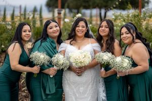 Bride poses with four bridesmaids in emerald green dresses holding white bouquets at a vineyard wedding.