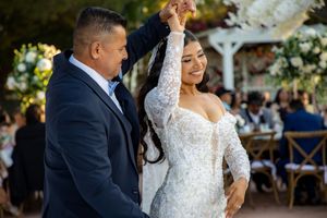 Father twirls bride in long-sleeve lace wedding gown during father-daughter dance at reception.