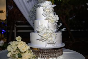 Elegant three-tier white wedding cake adorned with large sugar roses cascading down the side.