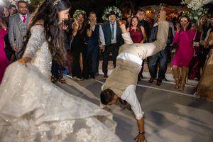 Bride in lace gown and groom perform acrobatic dance move at outdoor wedding reception.