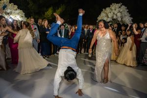 Guest in blue suit does handstand on wedding dance floor while bride watches and cheers.