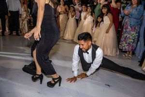 Groomsman performs splits on dance floor while female guest in black outfit looks on.