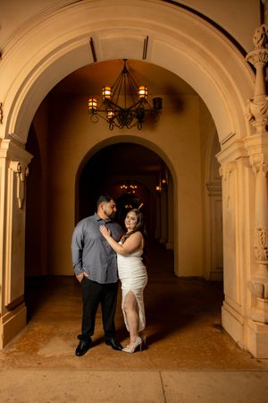 Romantic couple embraces under ornate golden archway during evening engagement photo session.