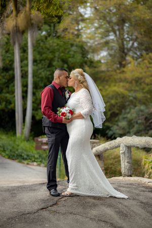 Bride and groom sharing a romantic kiss outdoors in a lush garden setting on their wedding day.