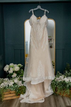 Elegant lace wedding gown with train hanging on a gold mirror in a decorated bridal suite.