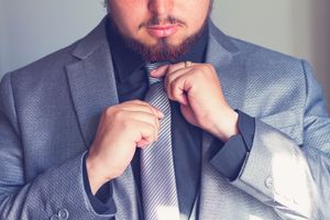 A man in a gray suit adjusting his striped tie, getting ready for a formal event.