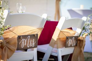 Wedding reception chairs decorated with burlap bows and Mr. and Mrs. signs for the newlyweds.