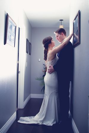 A bride and groom share a romantic moment in a hallway, with the bride in a white gown.
