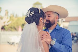 Bride and bearded groom in a cowboy hat share a close romantic moment at their outdoor wedding.
