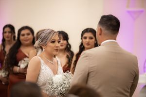 A bride in a lace gown holds baby's breath bouquet during her wedding ceremony at the altar.