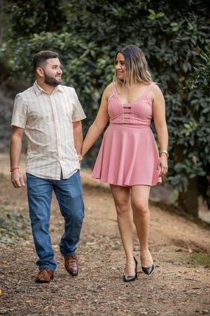 Smiling couple walks hand in hand on garden path, man in striped shirt, woman in pink mini dress.