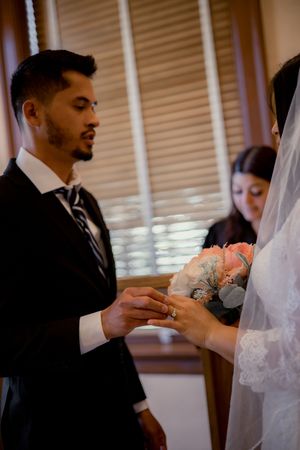 Groom in black suit placing wedding ring on brides finger during intimate ceremony.