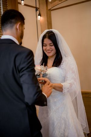 Radiant bride in lace gown smiling joyfully while exchanging rings with groom at ceremony.