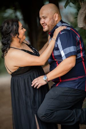 Happy couple laughs and dances together outdoors, woman in black gown, man in plaid shirt.