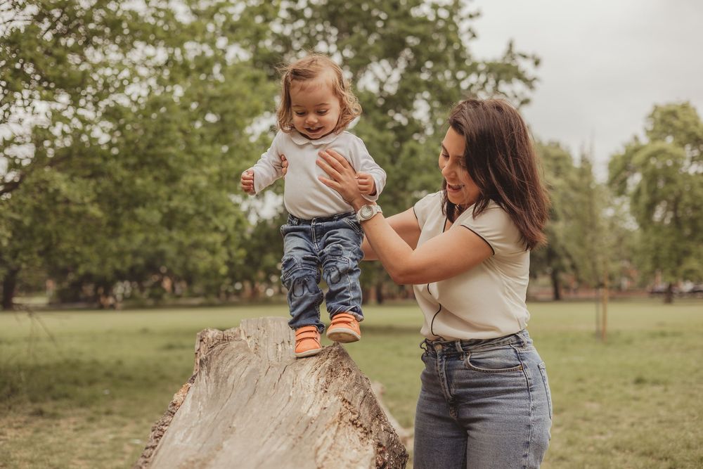mum helping toddler to walk across a log