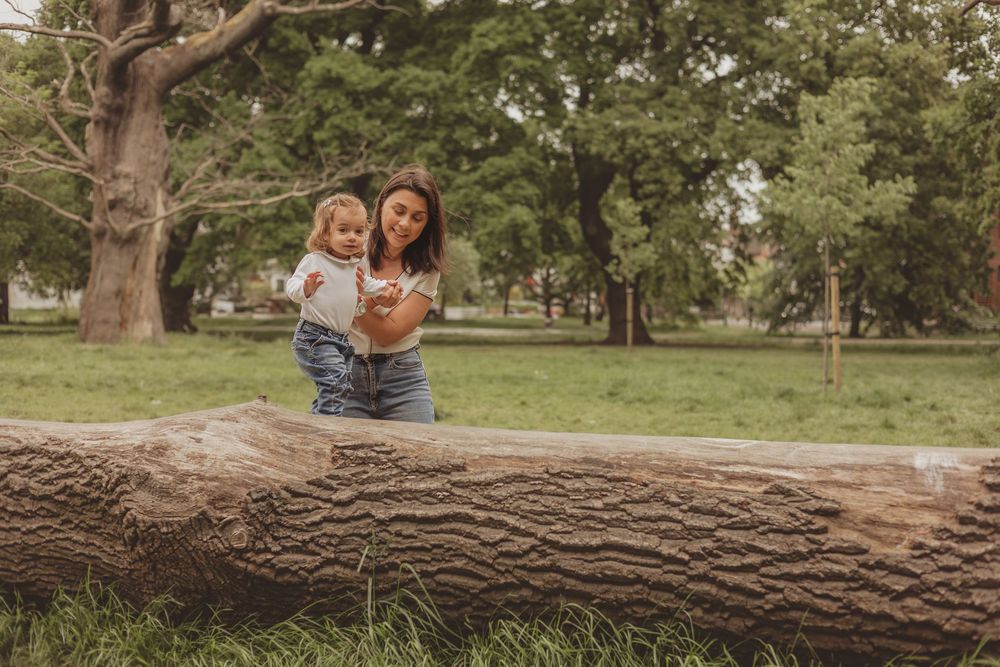 mum helping toddler to walk across a log