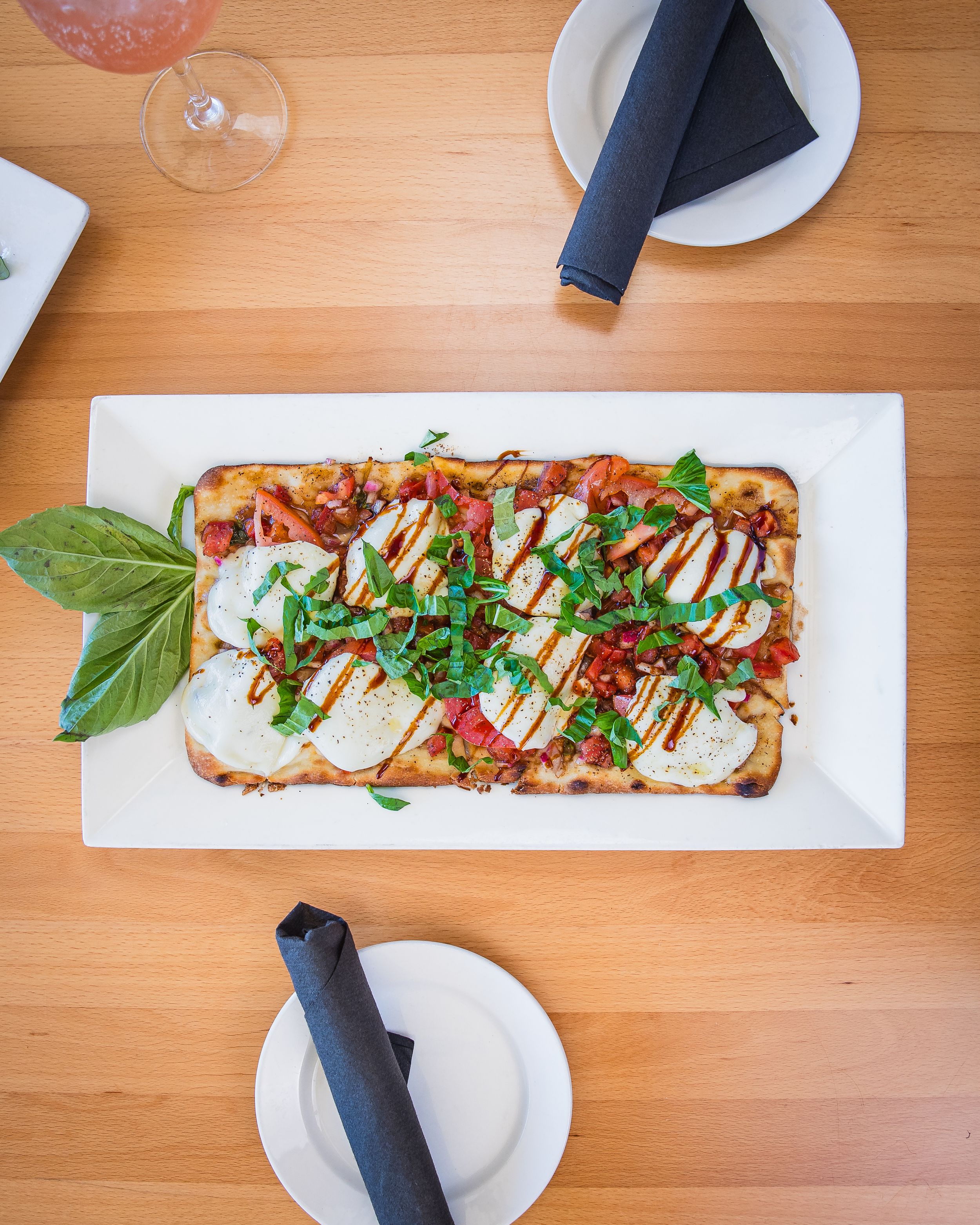 Gourmet flatbread topped with prosciutto, arugula, and drizzles of balsamic glaze served on white plate on wooden table.