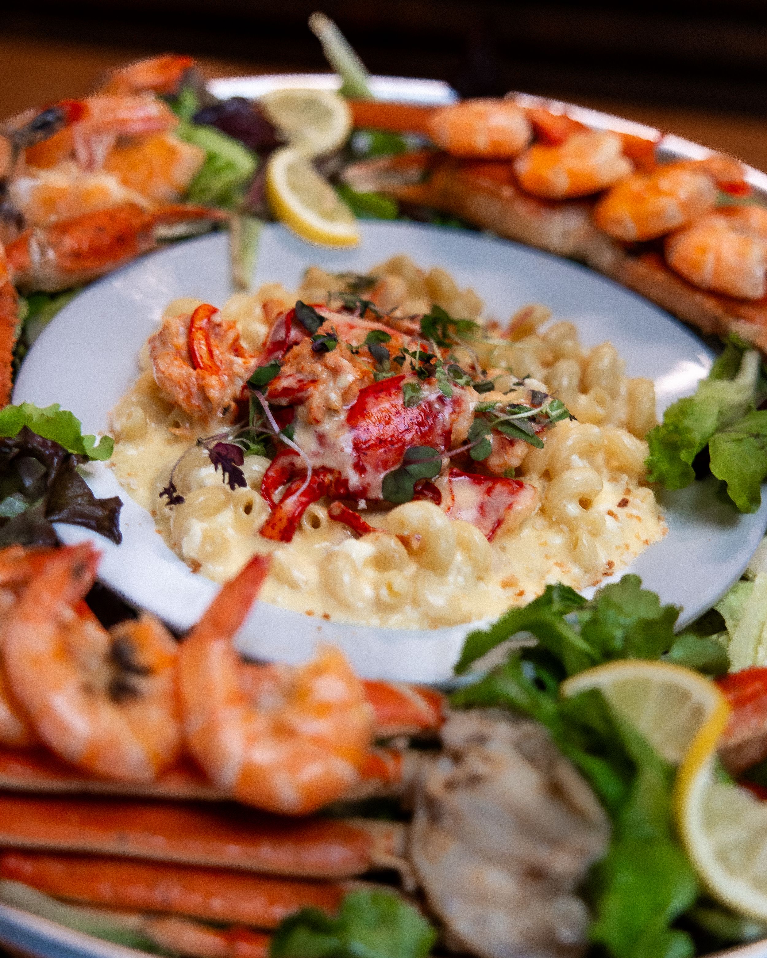 Elegant seafood platter with grilled shrimp, crab legs, and creamy lobster mac and cheese garnished with fresh herbs and lemon.