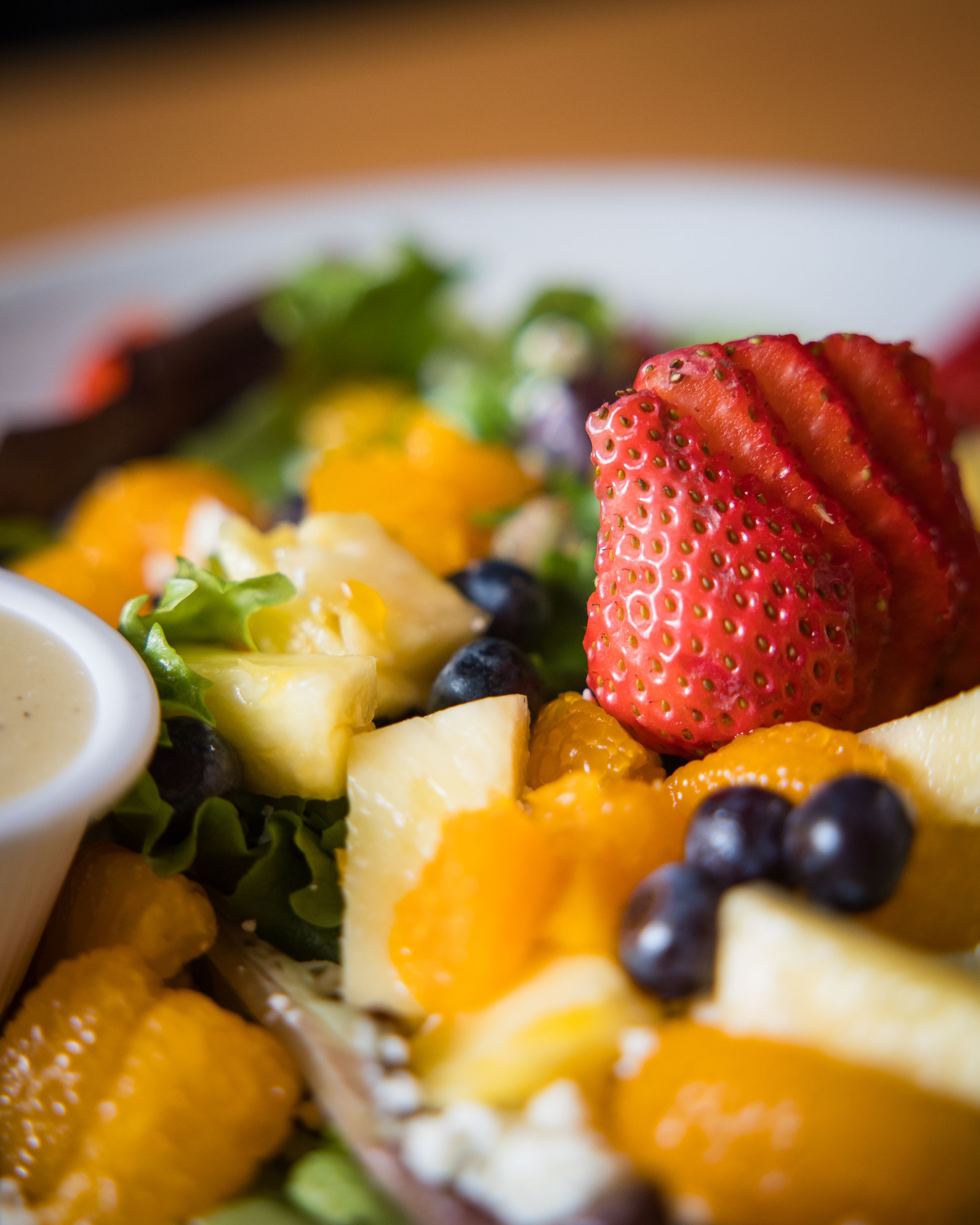 Fresh fruit salad with vibrant strawberries, mangos, blueberries and pineapple served on a white plate with dressing.
