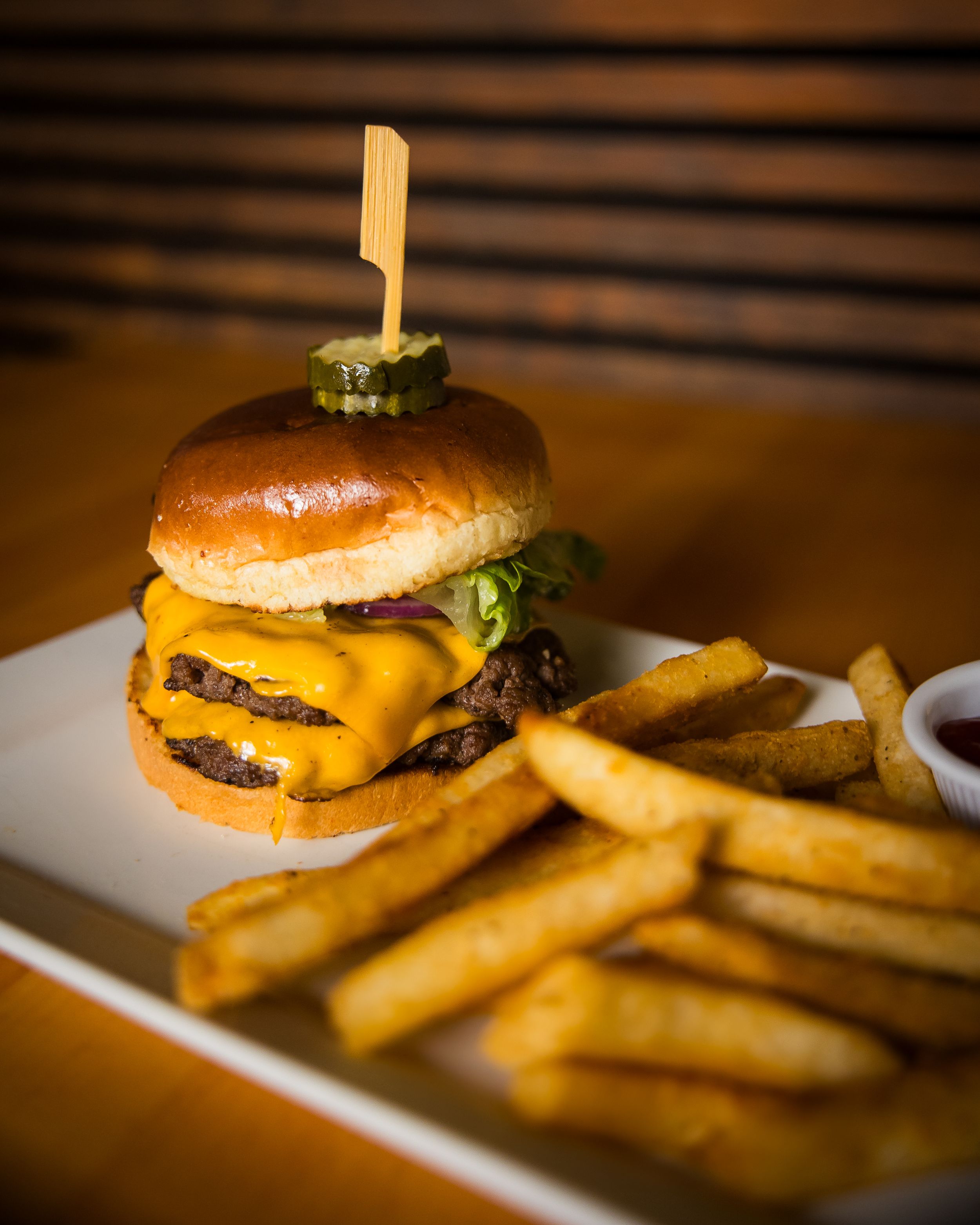 Juicy cheeseburger with melted cheese and crispy french fries served on a white plate in warm lighting.