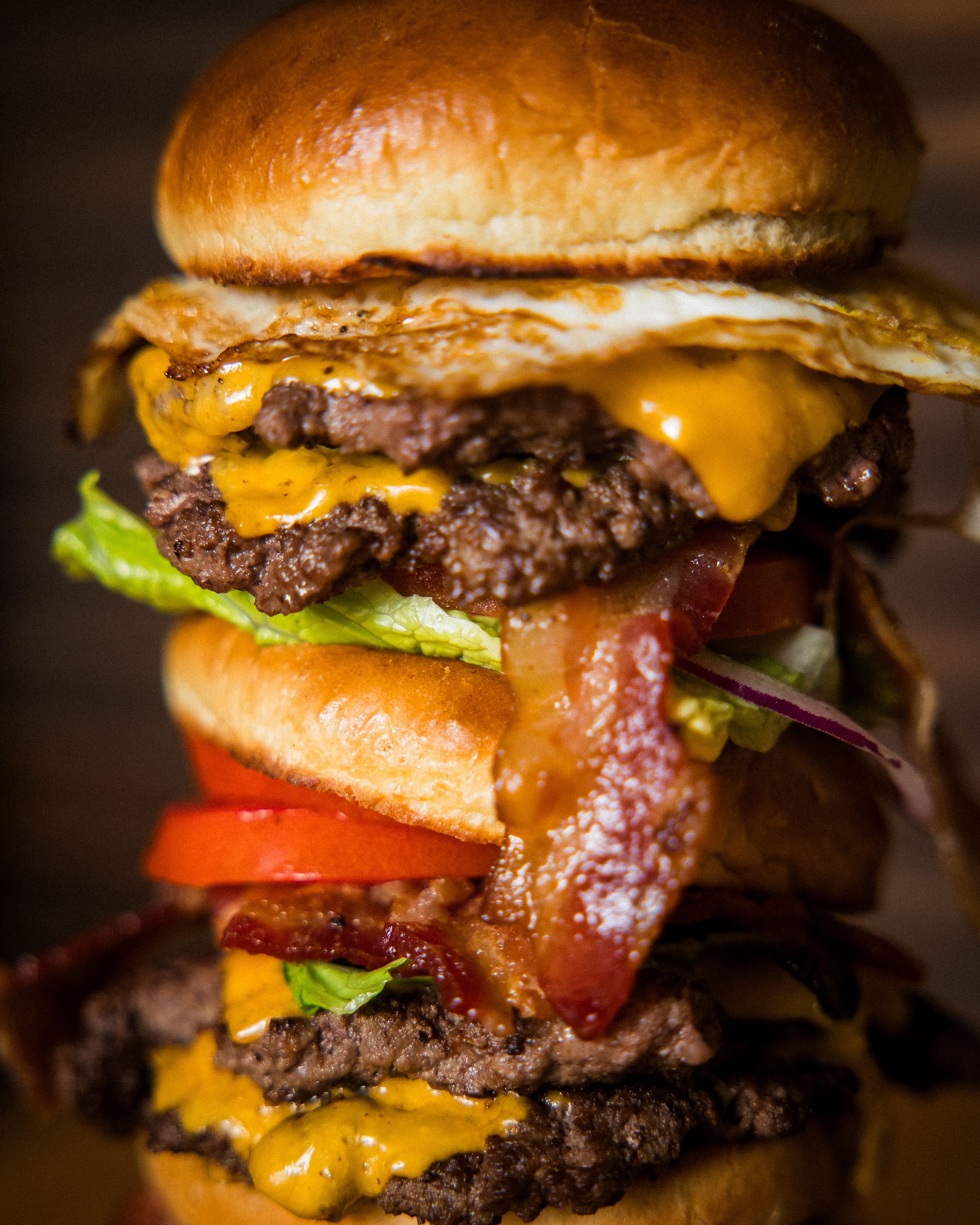 Close-up shot of a juicy double cheeseburger stacked with bacon, lettuce, tomato and melted cheese on a toasted bun.