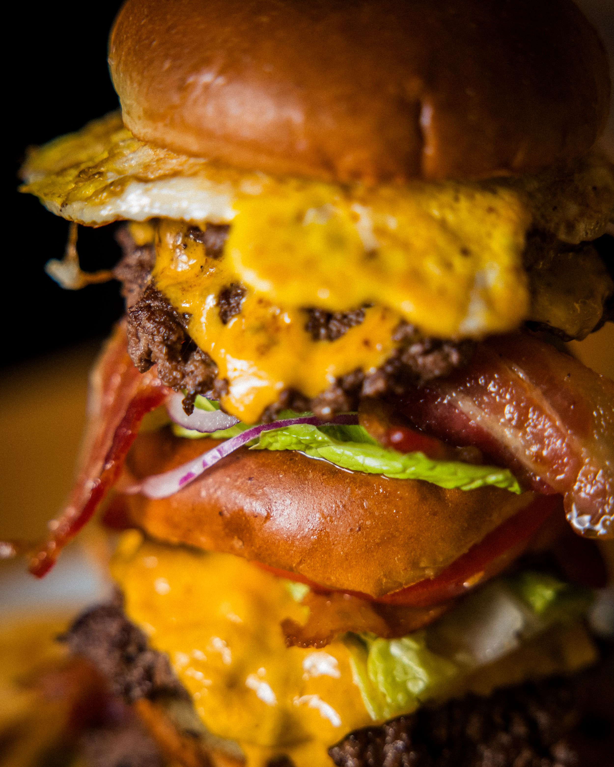 Close up of a juicy double cheeseburger with melted cheese, bacon and lettuce on a glossy brioche bun.