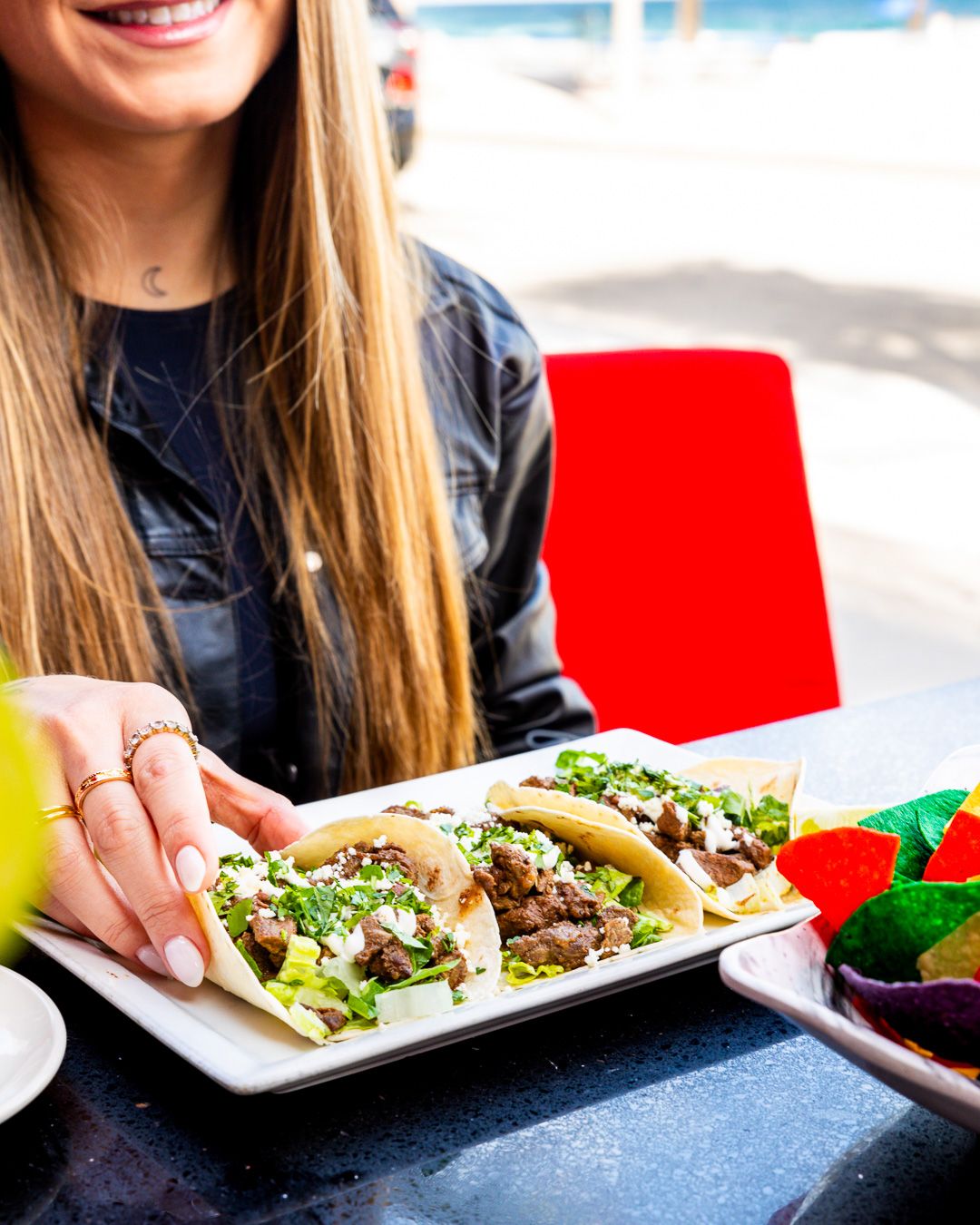 Street style tacos garnished with fresh herbs served on a white plate with chips and salsa on the side.