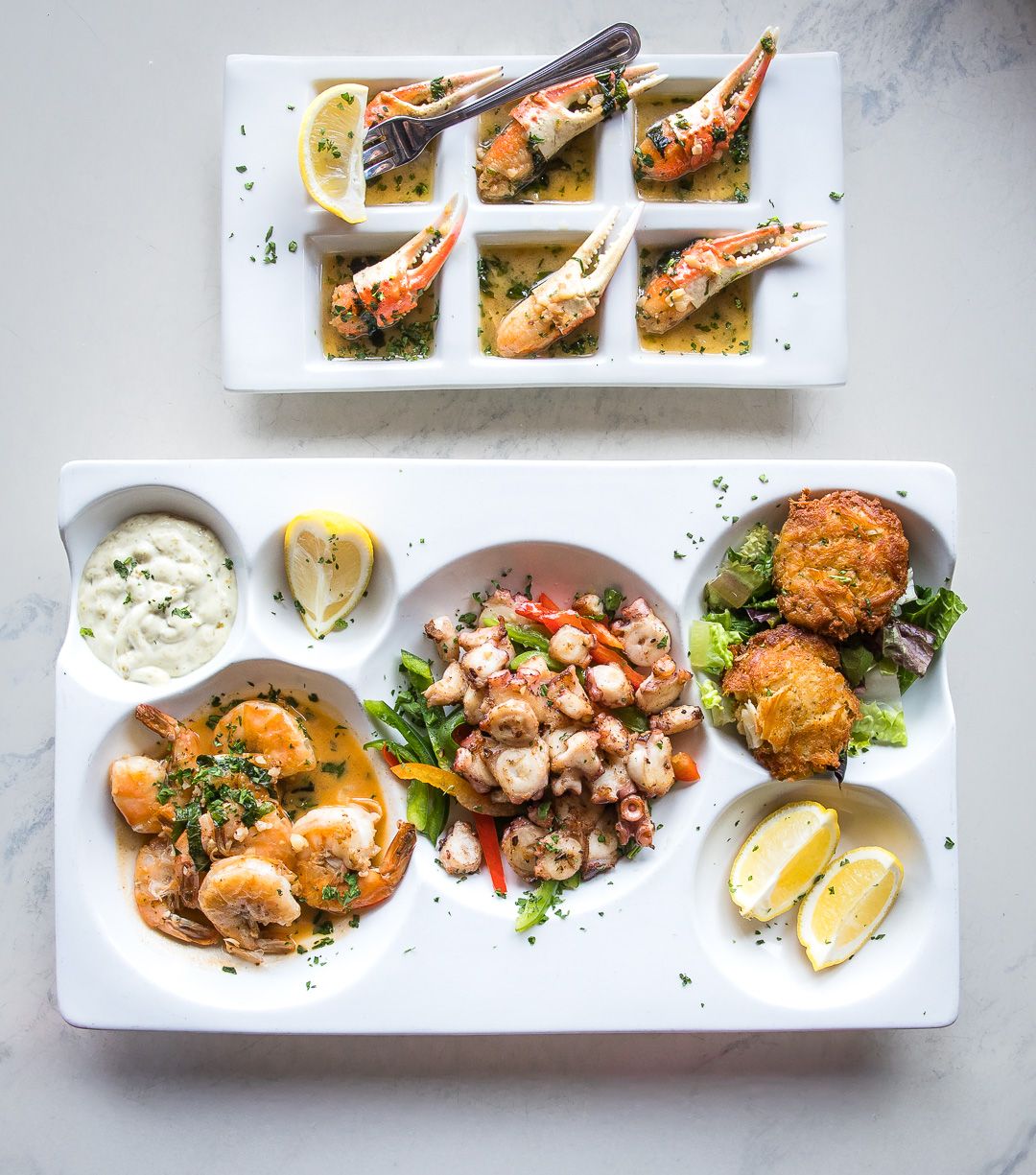 Elegant seafood platter featuring grilled shrimp appetizers, octopus, and various seafood dishes with complementary sauces and garnishes.