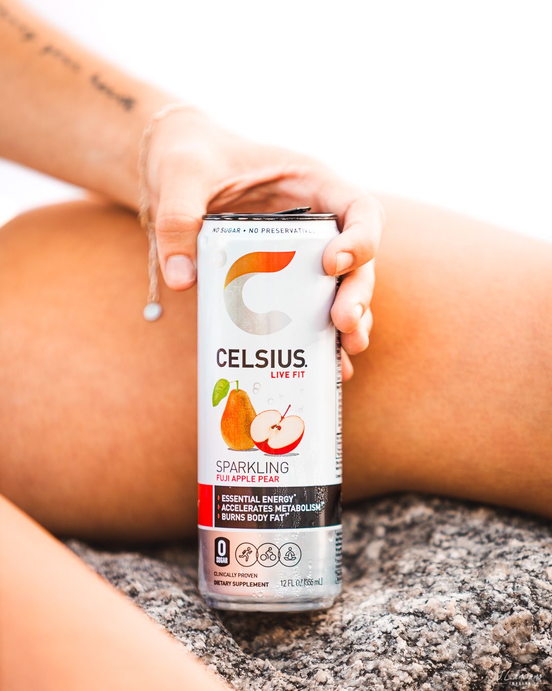 Celsius energy drink can featuring apple flavor being held against a stone surface.