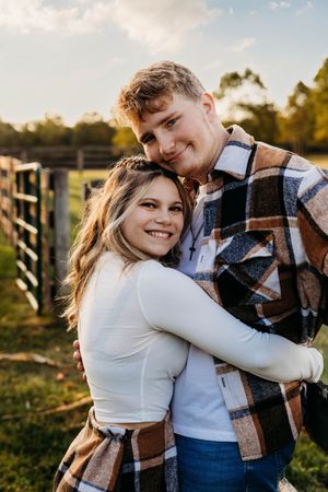 A couple embraces outdoors during golden hour wearing casual clothing and sharing intimate moments together.